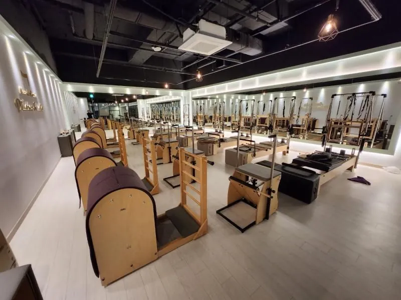원목 필라테스 기구가 줄지어 놓인 넓은 스튜디오